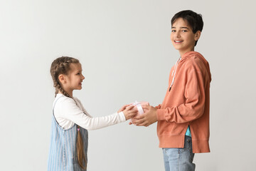 Little boy greeting his sister with gift on light background. Children's Day celebration