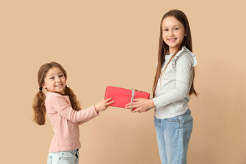 Little girl greeting her sister with gift on beige background. Children's Day celebration
