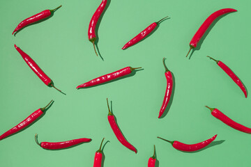 Creative pattern made of red hot chili peppers on pastel green background. Minimal flat lay.