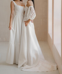 Fototapeta na wymiar Two models or brides dressed in the classic white wedding dress. Cown with cleavage, long fancy sleeves. Gorgeous classic sleeveless wedding dress