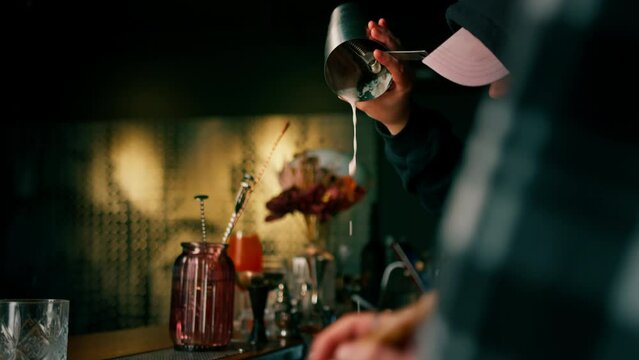 two young bartenders preparing alcoholic cocktails at the bar mixing ingredients working in pairs at a party