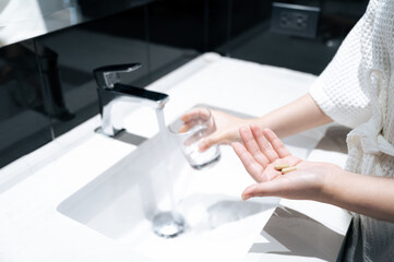 Pills on one hand and another hand hold glass for get water from basin faucet in bathroom, take pills concept.