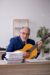 Obraz premium Old male employee playing guitar at workplace