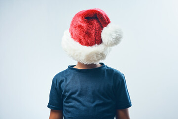 Fototapeta na wymiar Has anyone seen my hat. Studio shot of a cute little boy covering his head with a Santa hat against a grey background.
