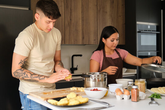Two young hispanic people moulding llapingachos dough and cooking in a pan at kitchen.