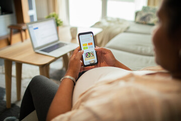 Young pregnant latina woman using a diet app on her smart phone while sitting on a couch in the living room of her home