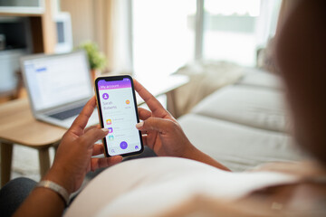 Young pregnant latina woman using a banking app on the couch in the living room