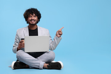 Smiling man with laptop on light blue background, space for text