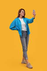 Beautiful woman in eyeglasses taking selfie on orange background