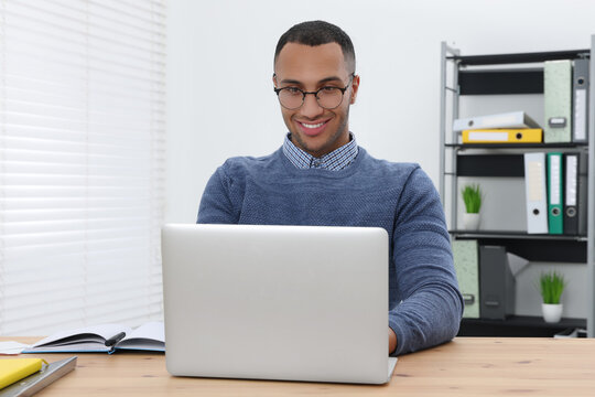 Happy young intern working with laptop at table in modern office
