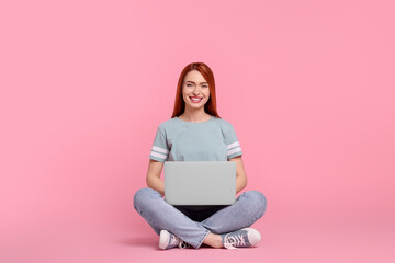 Naklejka premium Smiling young woman working with laptop on pink background