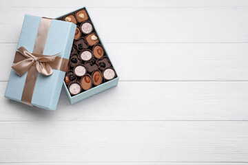 Open box of delicious chocolate candies on white wooden table, top view. Space for text