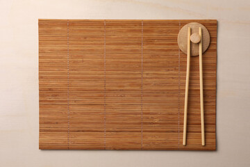 Bamboo mat and chopsticks on beige table, top view. Space for text