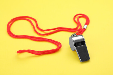 One metal whistle with red cord on yellow background