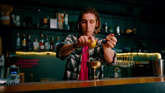 Male hands of a bartender rub the peel of an orange fruit for a cocktail with a special grater tool close-up