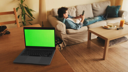 Laptop with green chromo key on the screen, mock-up screen, stands on table, in the background guy...