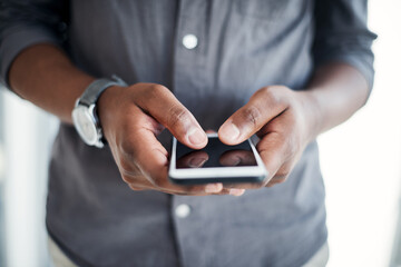 Maintaining a social presence is essential in business. an unrecognizable businessman standing alone in his office and using his cellphone.