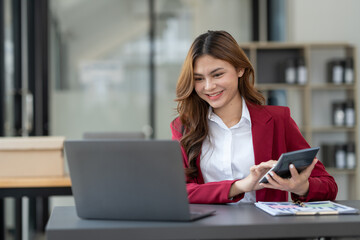 Beautiful asian businesswoman working on laptop and calculating with financial calculator from statistics data graphs, charts. Successful business results in modern office with joy.