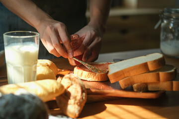Obraz premium Cropped image of man making sweet sandwich and spreading strawberry jam on bread.
