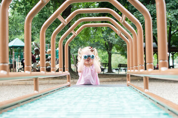 Cute Caucasian toddler girl looking through binoculars on the playground. Exploring concept	
