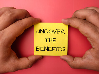Hand holding note paper with the word UNCOVER THE BENEFIT