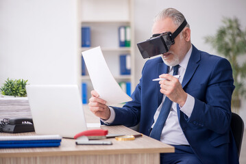 Old male employee wearing virtual glasses at workplace