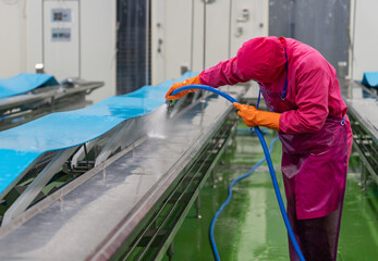 Worker use high pressure water spray cleaning conveyor belt after finishing daily job