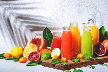 Summer fruit juices and smoothies, food background. Mix of different whole and cut fruits: orange, grapefruit, lime, tangerine with leaves and bottles with drinks