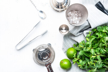 Mojito cocktail making. Mint, lime, ice - ingredients and steel bar tools. Top view, white table background, copy space