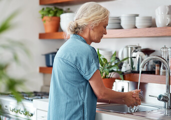 Your health is in your hands. a mature woman washing her hands in the kitchen sink at home.