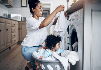 She loves clean laundry. a young mother playfully bonding with her baby girl while doing the...