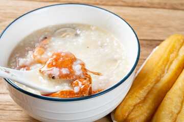 spoon taking out crab from seafood porridge with deep-fried dough sticks nearby