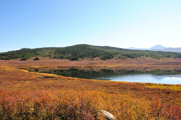 A fragment of a beautiful calm lake in a lowland surrounded by hills overgrown with yellowed grass on an autumn sunny day.