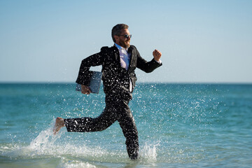 Business man in suit with laptop running in sea water. Travel tourism and business concept. Crazy...