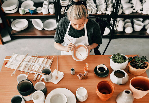 Making sure its perfect. High angle shot of an unrecognizable woman sitting alone and painting a pottery bowl in her workshop.