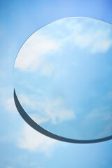 Abstract minimal scene with round mirror placed on blue background. The mirror reflects the clear...