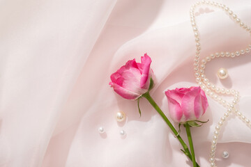Against a white chiffon fabric background, Roses are decorated with pearls and pearl necklace. Rose (Rosa) essential oil has many beneficial properties