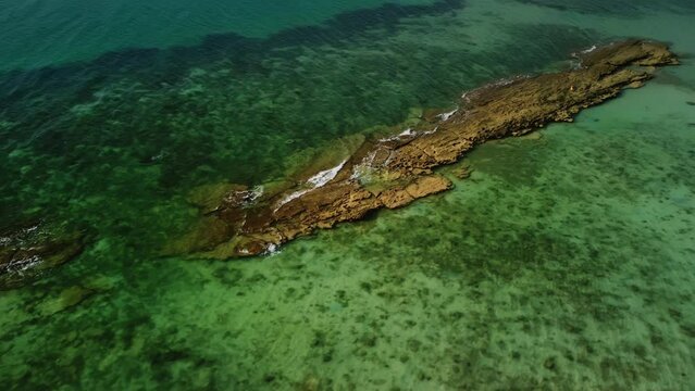 Aerial top view of rock shoal in the sea filmed by drone at summer day. View on shallow ocean with weed on bottom which makes it of green color. Concept of tropical nature. Theme of the seascape