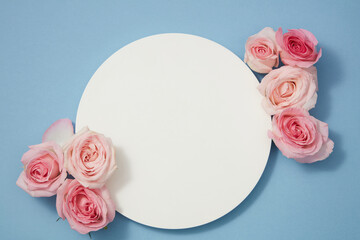 Fototapeta na wymiar Minimal concept, top view of features delicate roses arranged on blue background with an empty round white podium for promotional messages or branding and cosmetic product presentation