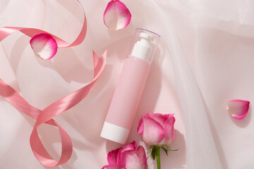 Unlabeled pump bottle dispenser with transparent cap arranged with Rose petals and pink ribbons. Rose (Rosa) has become increasingly popular as an ingredient in skincare