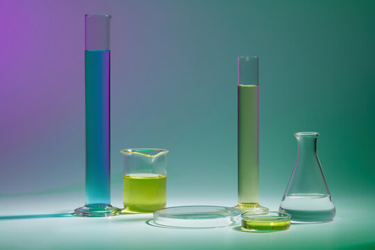 Abstract background with laboratory concept - lab glassware containing color liquid and round transparent podium for cosmetic product presentation on color background.