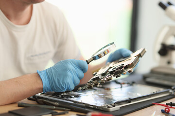 Man looks at printed circuit board through magnifier glass