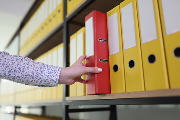 Hand of woman taking red ring binder from office archive