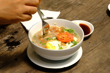 a hand holding a spoon, scooping up noodle soup. noodles with free-range chicken, egg, sliced ​​tomatoes. Indonesian food.