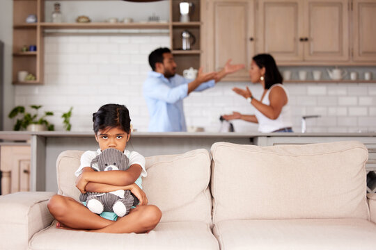 Afraid little girl holding a teddy in an abusive household. Young couple fighting while their child sits on the couch