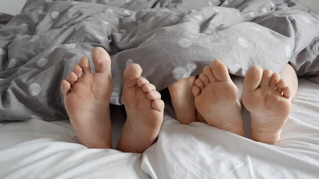 Close-up footage of happy parents and their child's feet under the blanket. Captures the warmth and love of family life