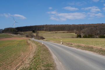 Road in the landscape with agricultural fields, trees and a blue sunny sky in spring