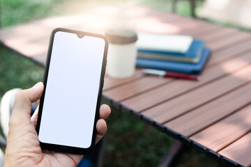 In relax time a man hand holding smart phone use to connect people and business with coffee cup and book on wooden table, outdoors cafe background