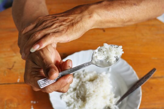 Elderly man is holding his hand while eating because Parkinson's disease.Tremor is most symptom and make a trouble for doing activities such as eat.Health care or elderly concept.Top view.