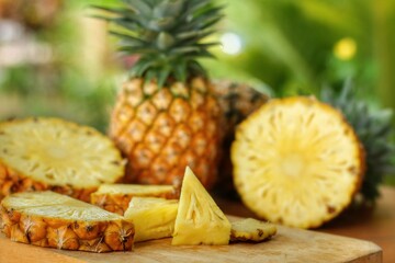 Fototapeta na wymiar Sliced and half of Pineapple(Ananas comosus) on wooden table with blurred garden background.Sweet,sour and juicy taste.Have a lot of fiber,vitamins C and minerals.Fruits or healthcare concept.